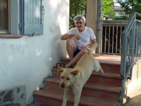 sorridente uomo brizzolato, seduto sugli scalini con il suo cane-guida, in pantaloncini blu e maglietta bianca...io